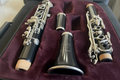 A black woodwind instrument set, including a clarinet barrel, mouthpiece, and part of a clarinet body, arranged in a black felt-lined case.